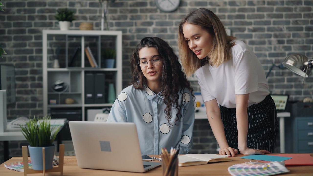 Two women working together on a laptop in a creative office space.
